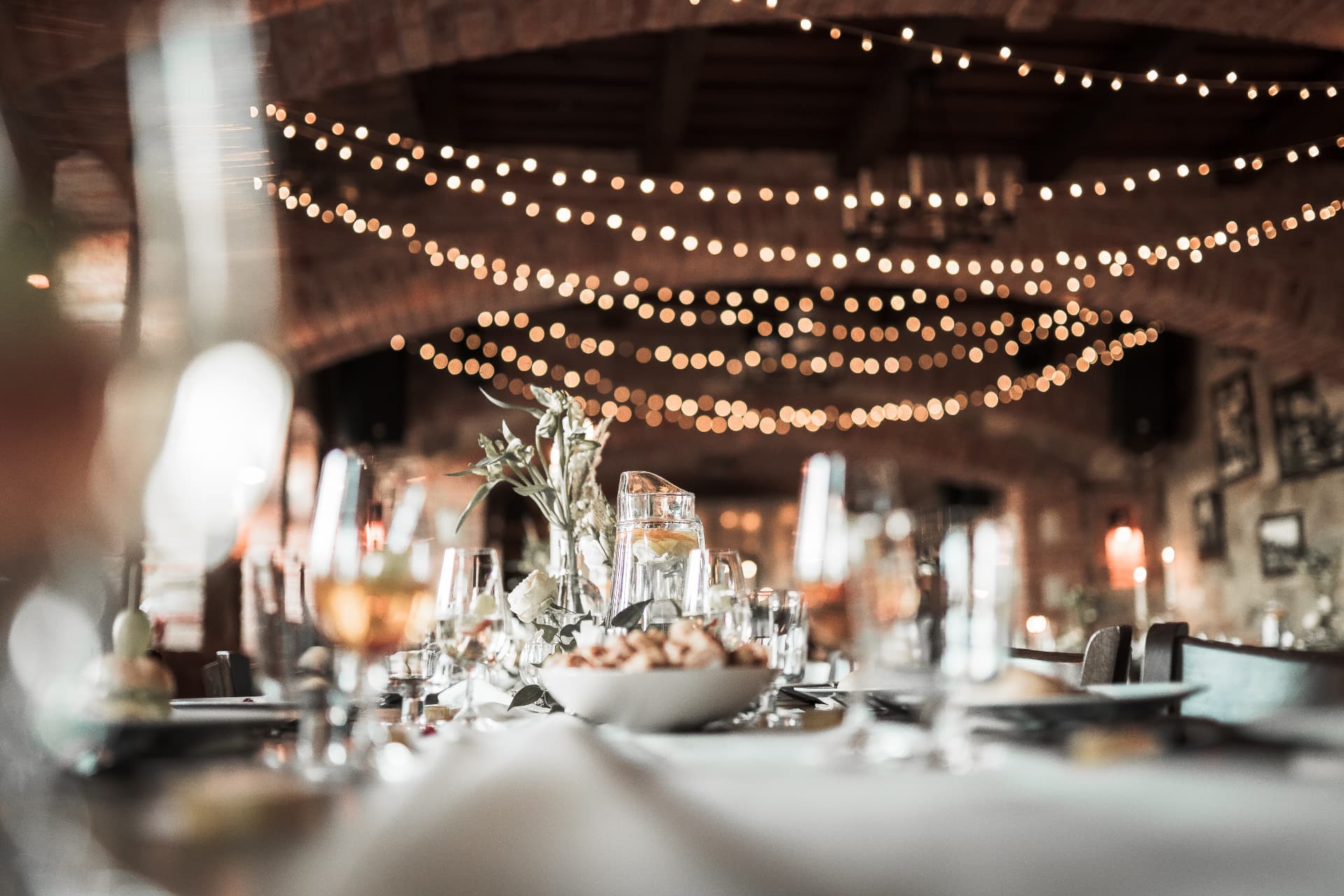 Festlich gedeckte Tafel mit Gläsern, Blumen und warmen Lichterketten im Saal