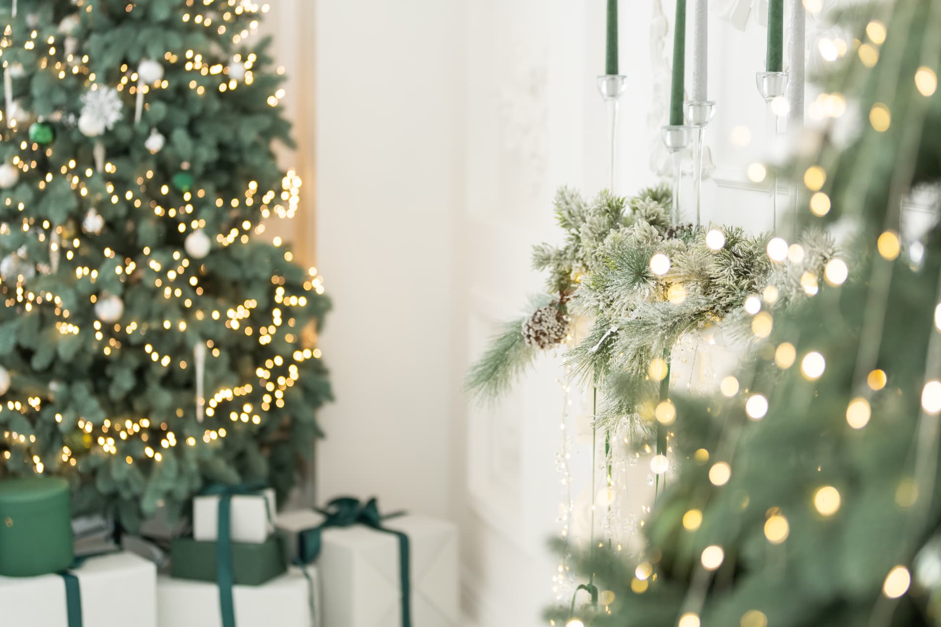 Festlich geschmückter Tannenbaum mit Lichterketten und Geschenken neben einer weiss gedeckten Konsole mit Tannengirlande, Tannenzapfen und dunkelgrünen Stabkerzen